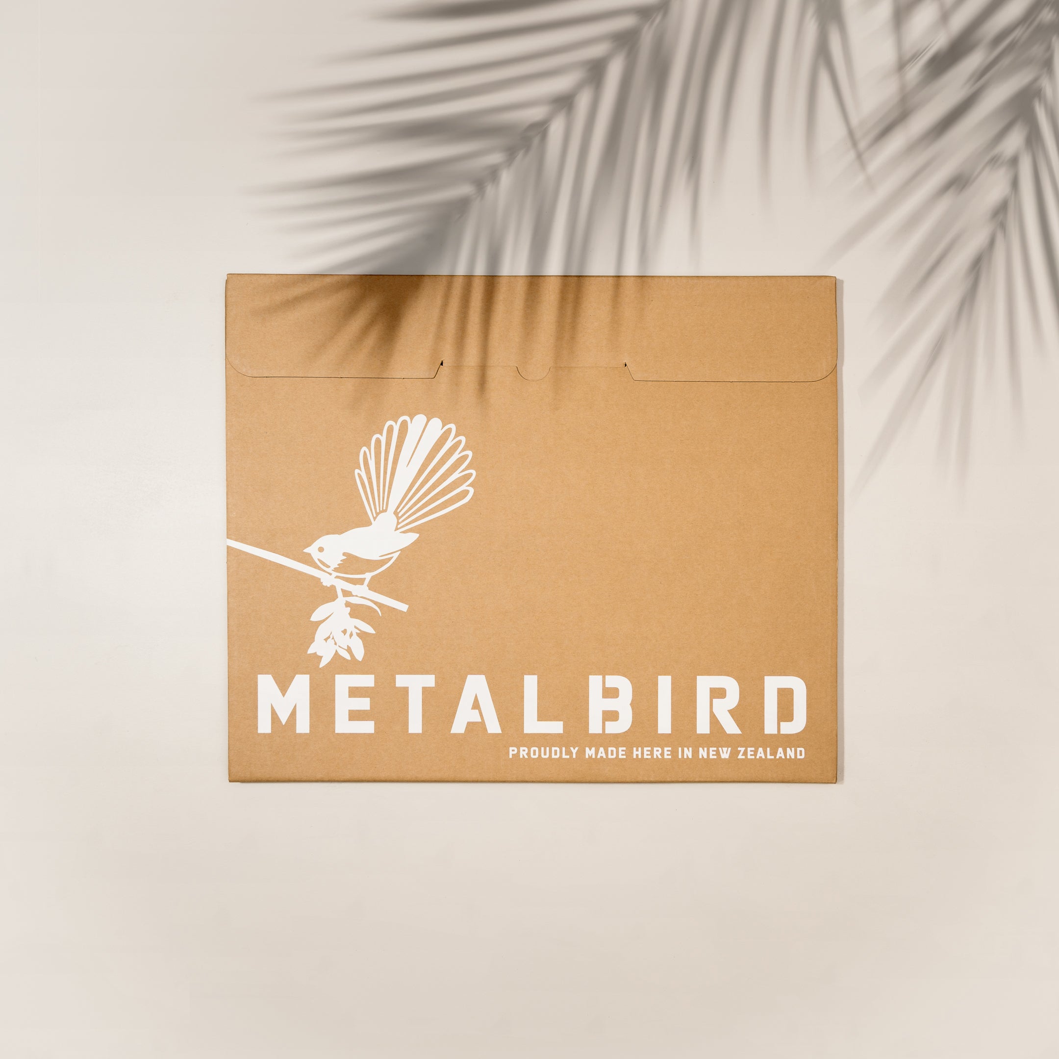 A brown cardboard envelope shows a white New Zealand Falcon on a branch, with “Kārearea: Wings of Glory” and Metalbird New Zealand branding. Palm leaf shadows cross this limited-edition Metalbird release.