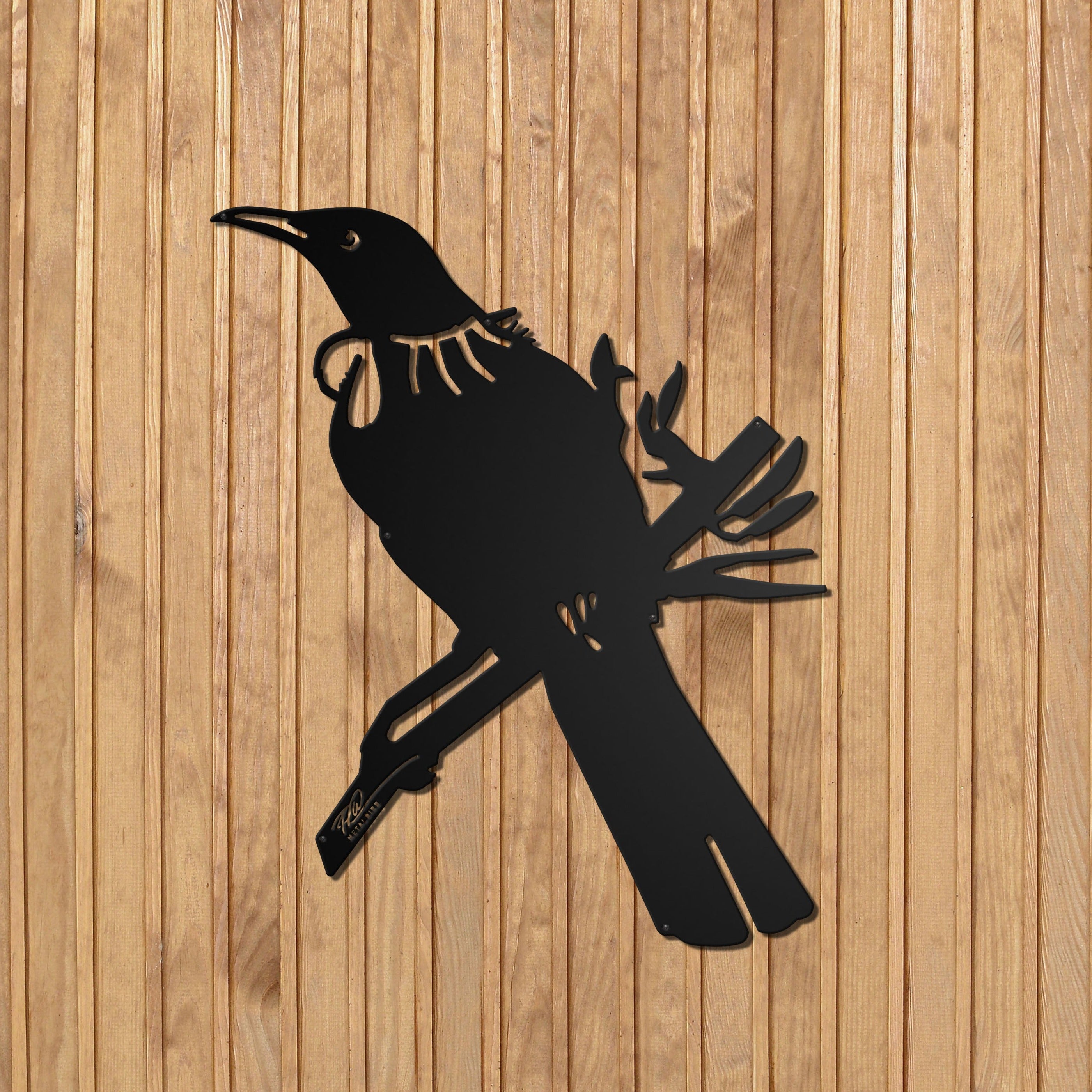 The Tūī Big Bird Wall Sculpture by Metalbird New Zealand features a premium black metal silhouette of a tūī with throat tufts, perched on a stylized branch and mounted on a vertical wooden wall, showcasing intricate cut-out details.