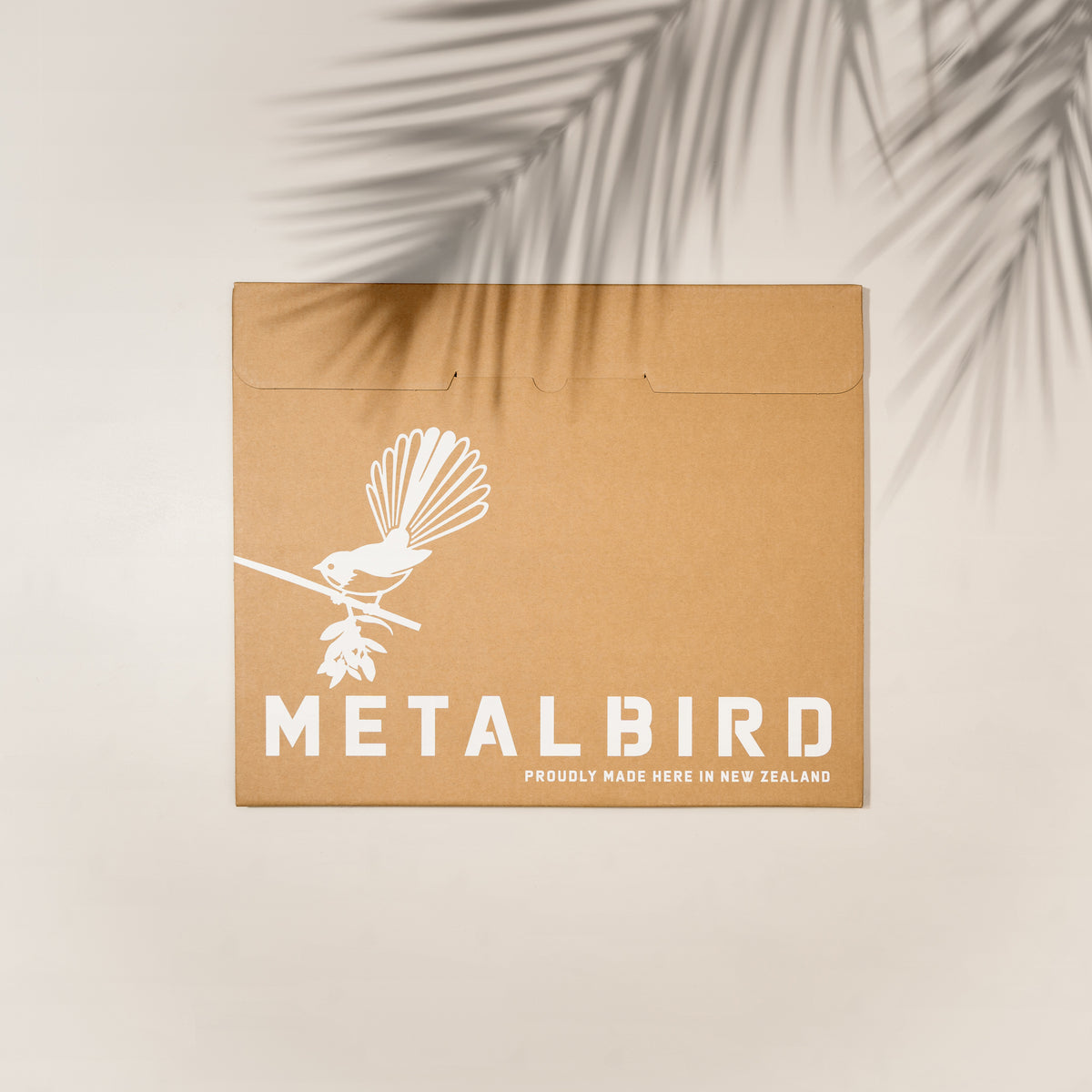 Closed brown Metalbird gift package beneath palm-leaf shadows.