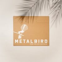 A brown cardboard envelope shows a white New Zealand Falcon on a branch, with “Kārearea: Wings of Glory” and Metalbird New Zealand branding. Palm leaf shadows cross this limited-edition Metalbird release.