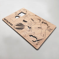 A thin, rectangular metal sheet labeled "Winged Hangers - 5 Festive Decorations" by Metalbird New Zealand rests on a light surface, showcasing multiple decorative bird silhouettes and photographed at an angle.