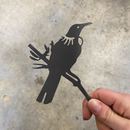A hand holds the Mini Tūī by Metalbird New Zealand, a flat black corten steel bird silhouette, perfect as unique yard art, seen against a blurred gray background.