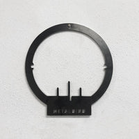 Mounted on a textured white wall, the Metalbird Seconds - PIWAKAWAKA AND BABY - XL by metalbird is a unique black metal circular wall decor featuring three vertical bars and METALBIRD cutout at the base, each with its own imperfections.