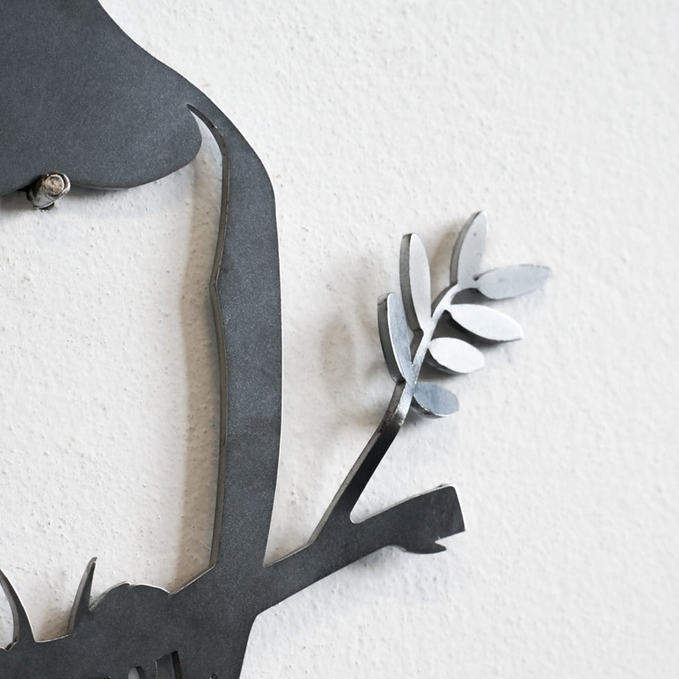 Close-up of a metalbird "Metalbird Seconds - PIWAKAWAKA AND BABY - XL" wall art piece, showing a black branch with leaves and birds, highlighting unique imperfections against a textured white wall.