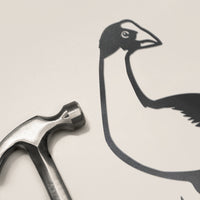 A silver hammer rests beside Metalbird New Zealand's flat, black corten steel Pūkeko bird cutout on a light beige surface—an ideal unique kiwiana gift.