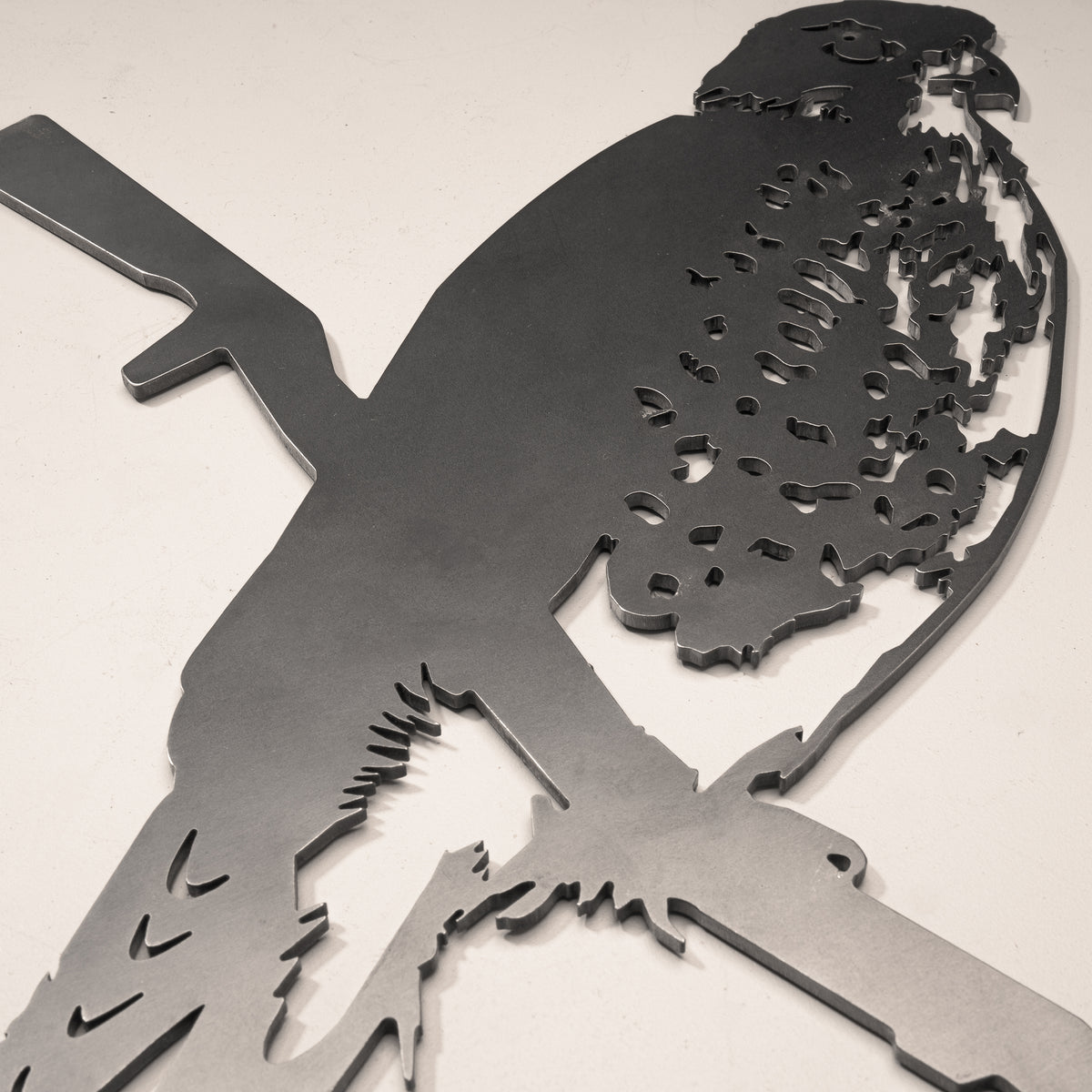 A close-up shows the Kārearea / New Zealand Falcon by Metalbird New Zealand, a steel silhouette of the falcon perched on a branch, beautifully crafted as metal wall art and displayed on a light surface.