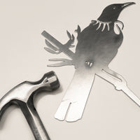 Raw Corten steel Tui bird sculpture beside a hammer, ready for easy installation as outdoor garden art in New Zealand