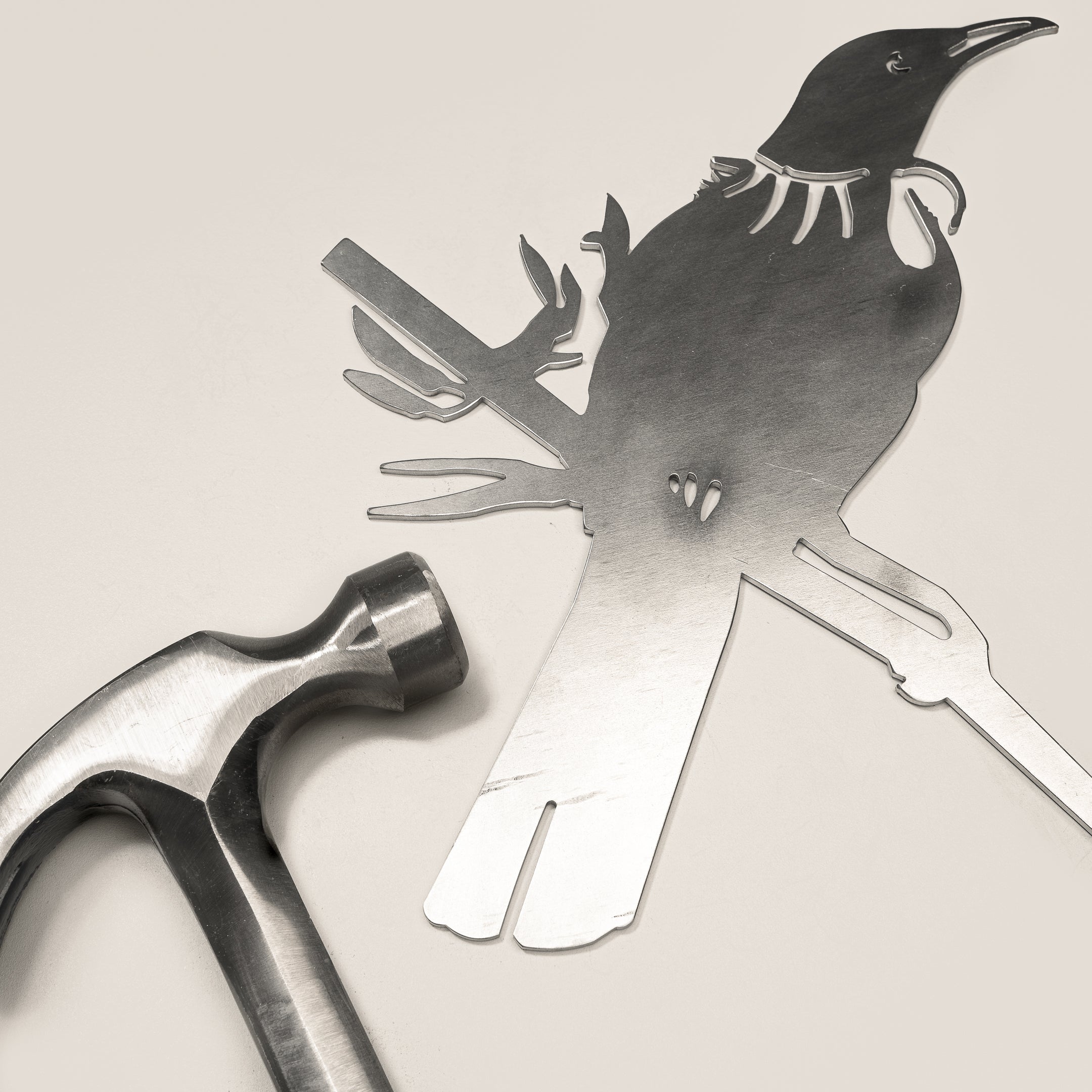 Raw Corten steel Tui bird sculpture beside a hammer, ready for easy installation as outdoor garden art in New Zealand