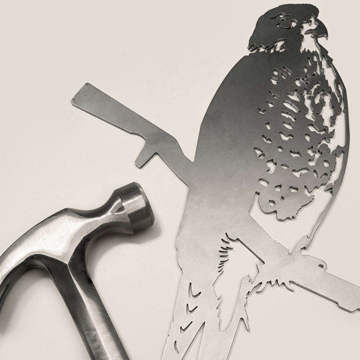 A metallic hammer rests beside the Metalbird New Zealand Kārearea / New Zealand Falcon steel silhouette, shaped like a perched bird of prey, both set against a light background.