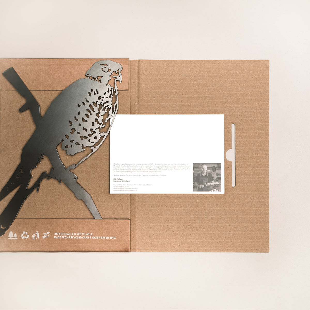 A cardboard folder holds a Metalbird New Zealand Kārearea / New Zealand Falcon steel silhouette on a branch, plus an insert with text and a black-and-white photo. The folder shows small printed text and symbols in the bottom left corner.