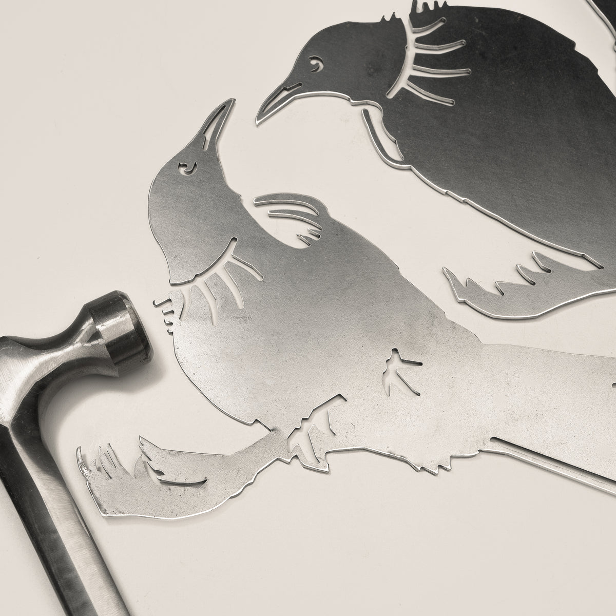 Tūī Twosome steel silhouette beside a hammer.