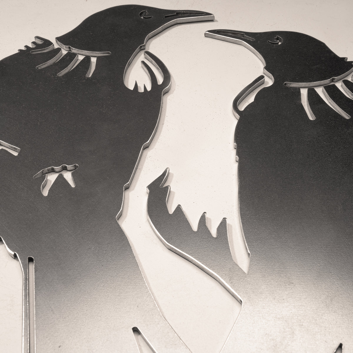 Close-up of two facing tūī heads and feather details in steel.