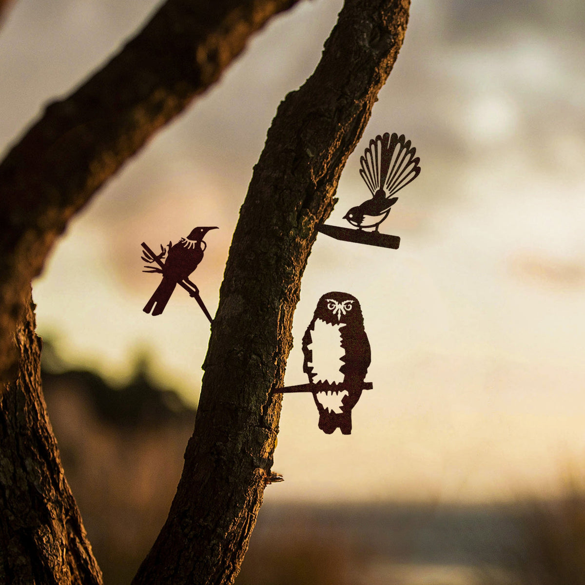 Three mini steel birds mounted on branches: tūī, fantail and ruru.